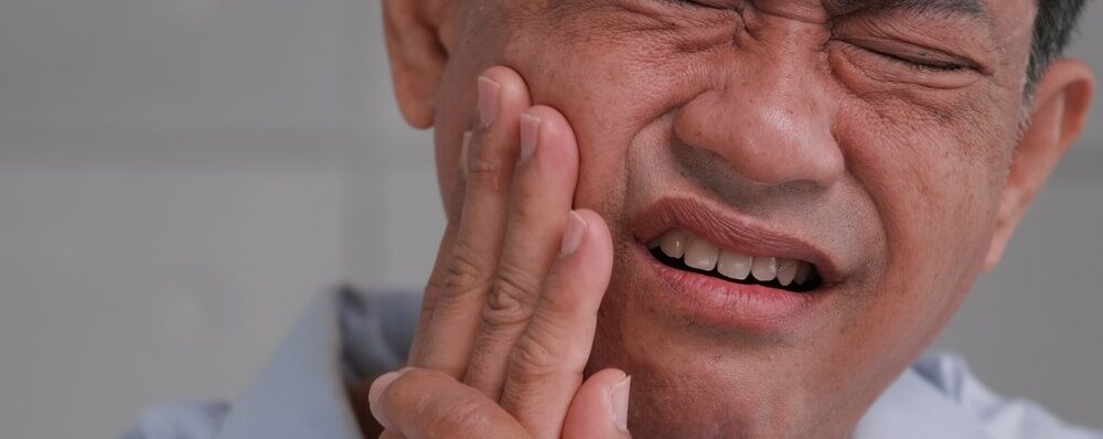 A man holds his right cheek and grimaces in pain due to tooth pain