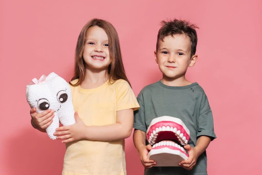 A smiling boy and a girl with healthy teeth hold a toy tooth in their hands on an isolated background.