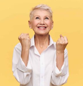 Older woman looks up, smiles, and pumps her fists in happiness.
