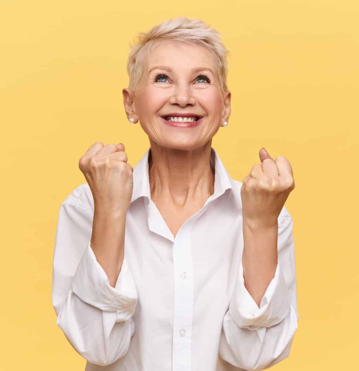 Older woman looks up, smiles, and pumps her fists in happiness.