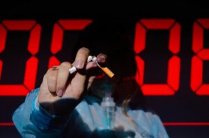 Silhouette of a woman crushing a cigarette between her fingers in front of a digital red clock, indicating anti-smoking.