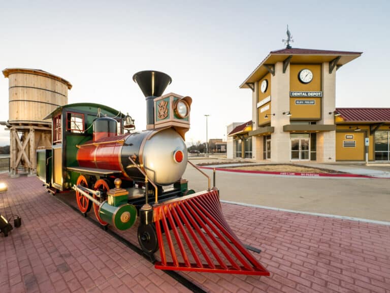 Exterior view of Dental Depot in Arlington with a large model train, clock tower, and yellow exterior.