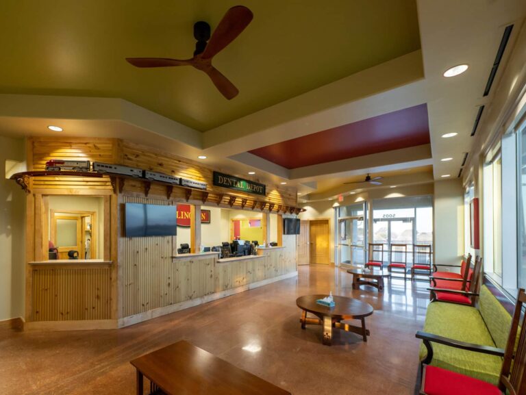 Interior view of the reception area and waiting room at Dental Depot in Arlington with light colored wood, multi colored chairs, and relaxed lighting.