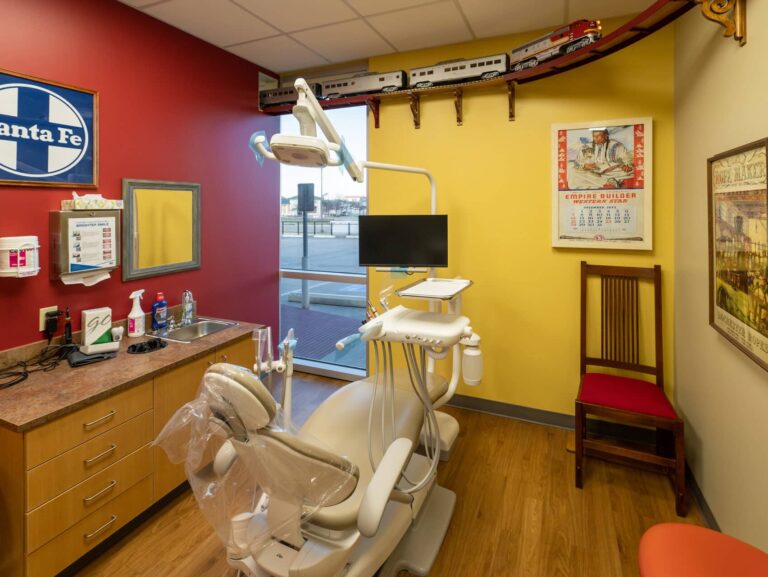 Interior view of a dental operatory in Arlington with red and yellow walls, a dental chair, and train themed signage.