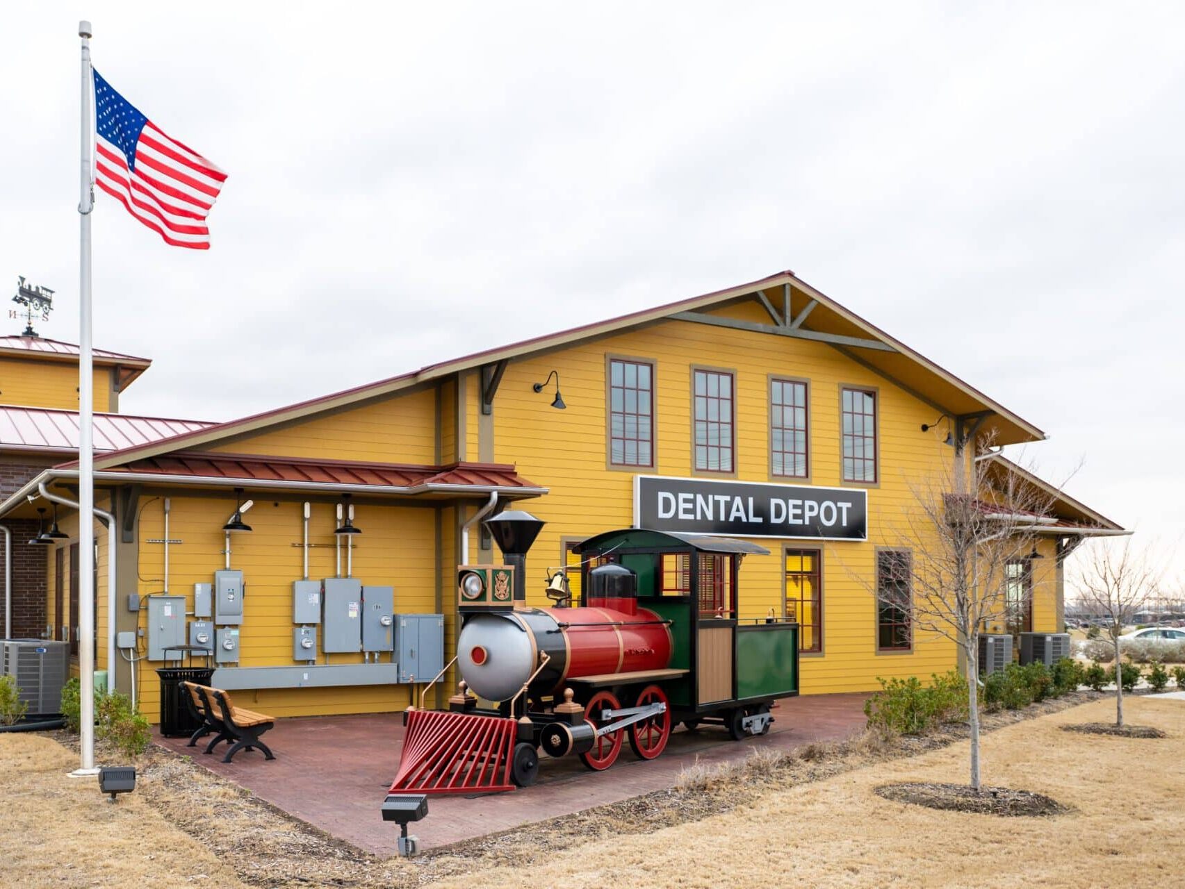 Exterior view of the Lewisville dentist office with a yellow exterior, flagpole, and model train.