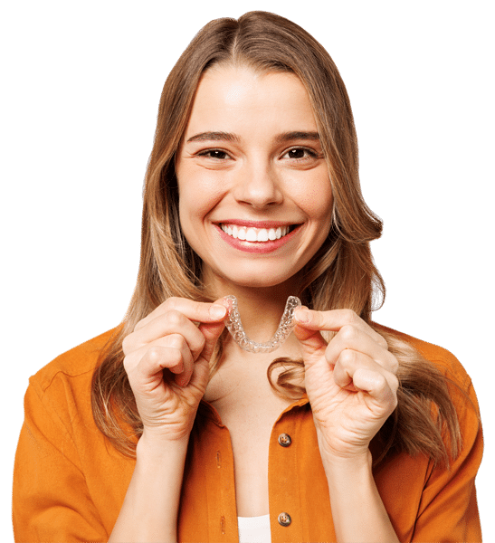 A young brunette woman in an orange shirt smiles while holding Invisalign aligners