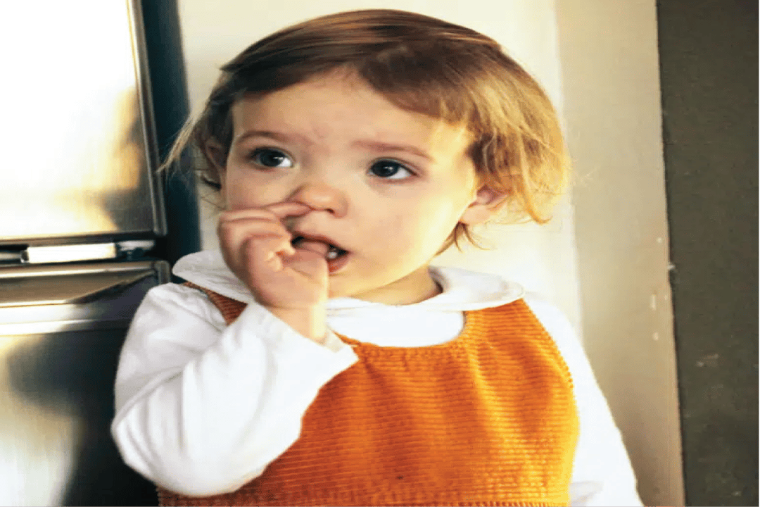 Little girl in orange and white dress sucking her thumb