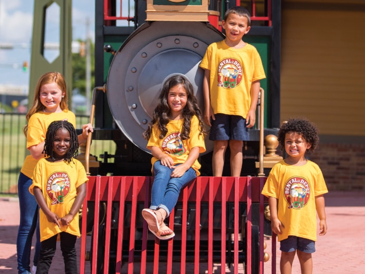 Kids in yellow Dental Depot t-shirts sit on the front of a train car outside the dental office.