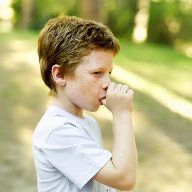 Little boy in light blue shirt standing outside sucking his thumb
