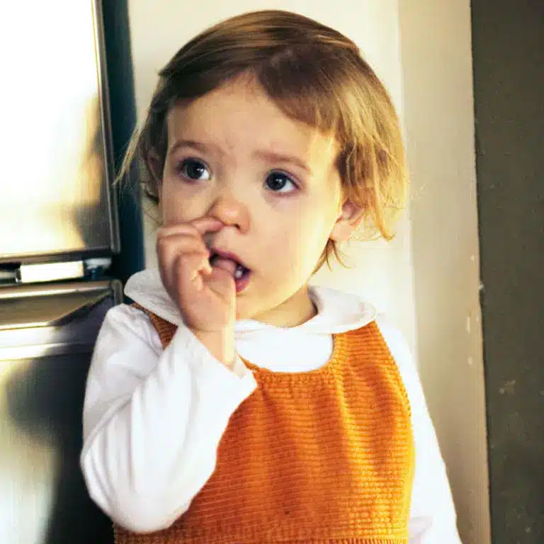 Little girl in orange and white dress sucking her thumb