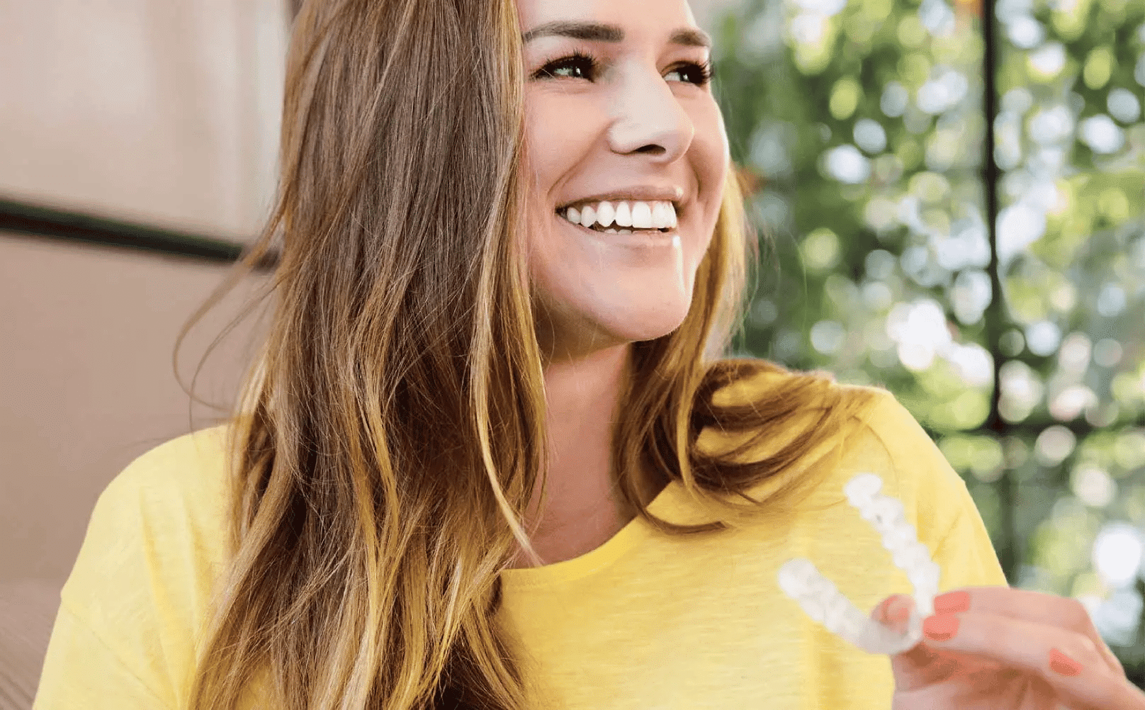 A young woman smiles while holding an Invisalign Aligner.